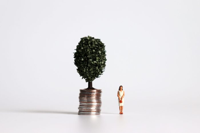 A miniature woman standing next to a pile of coins with trees.