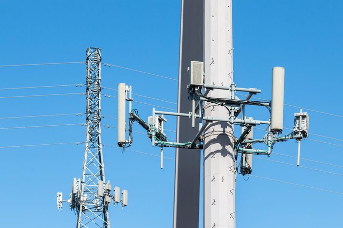 Cell tower antennas mounted on steel power poles close up. Lattice structure tower in blurred background. Blue sky.