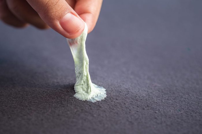 Close up hand removing sticky chewing gum from black textile or clothes