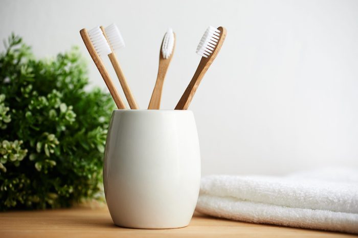 Four bamboo toothbrushes in a glass with copy space on a wooden background