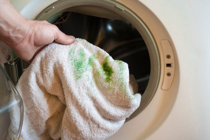 Man puts a dirty towel, stained with grass, in a washing machine