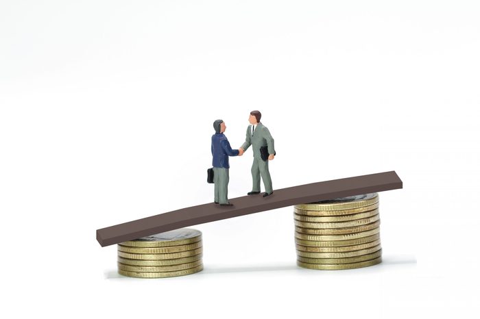 Miniature people, two businessmen shaking hand on the bridge between stack of coins, business concept
