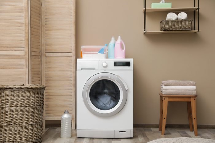 Modern washing machine near color wall in laundry room interior