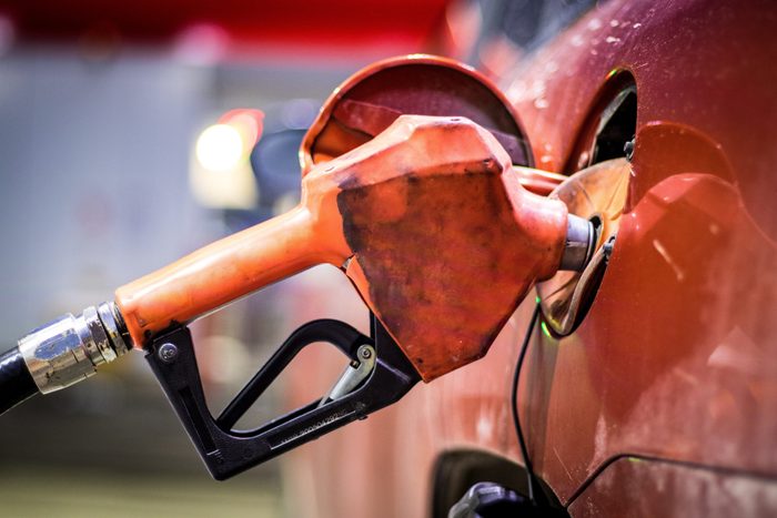 Red gas pump nozzle resting within the opened tank of a vehicle