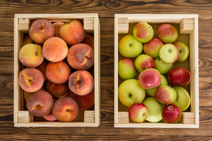 Small wooden crates of healthy fresh fruit filled with ripe peaches and variegated apples view from above on a table at farmers market