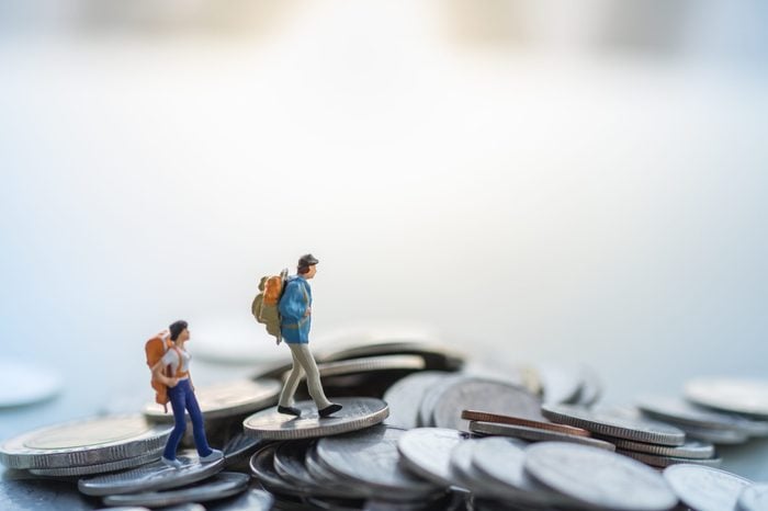 Travel and money concept. Two traveler miniature figures with backpack walkig on pile of coins.