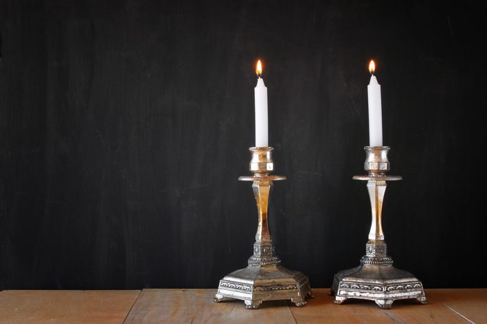 Two candlesticks with burning candles over wooden table and blackboard background