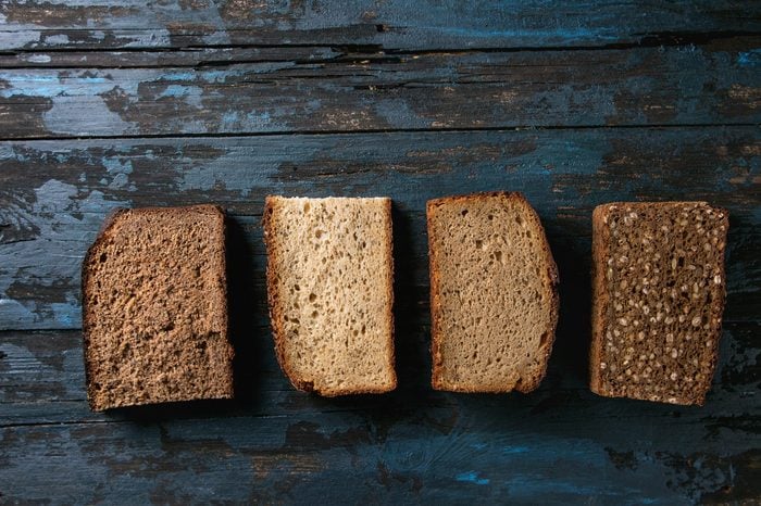 Variety loaves of sliced homemade rye bread whole grain and seeds over old dark wooden background. Top view, space. Healthy eating