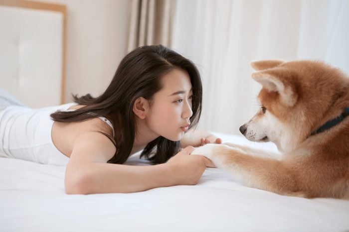 Young asian woman lying on bed, playing with pet dog.