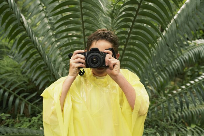 Young boy in raincoat taking photos in forest during field trip