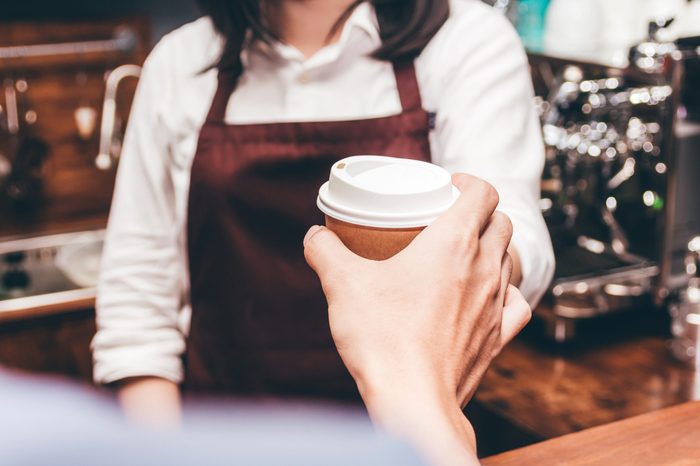 Woman barista giving coffee cup to customer at cafe