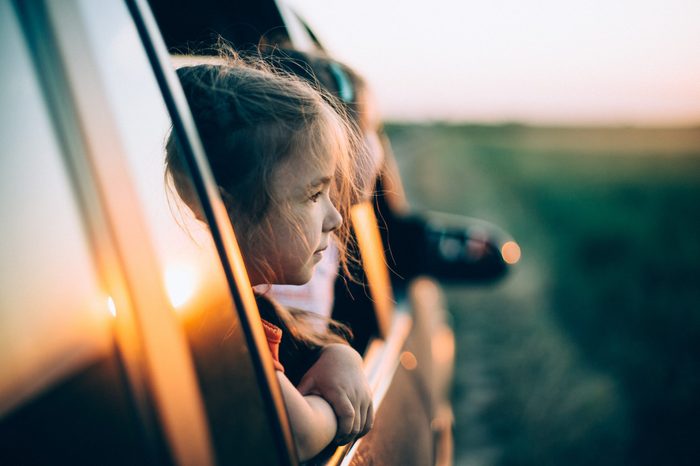 Two little girls peeks out of the car in the sunset