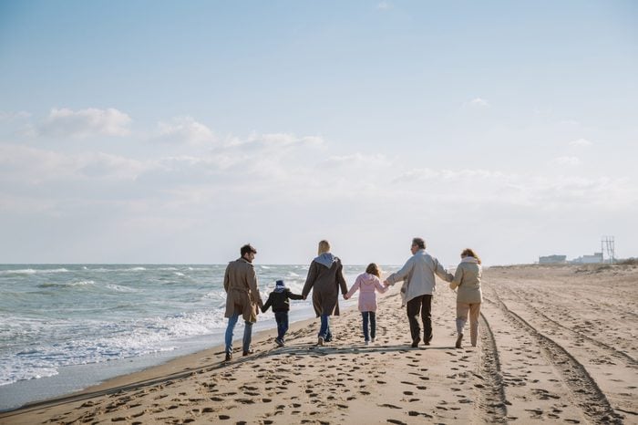 back view of big multigenerational family walking together on seashore