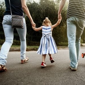 happy stylish parents holding hands with daughter and walking in sunny street, amazing family moment. father's mother's day