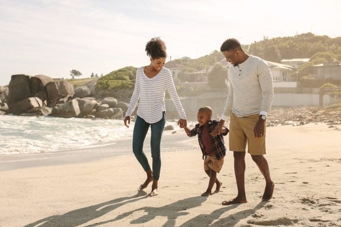 Family of three taking a walk along the sea shore. Man and woman holding hands of son and walking on beach.