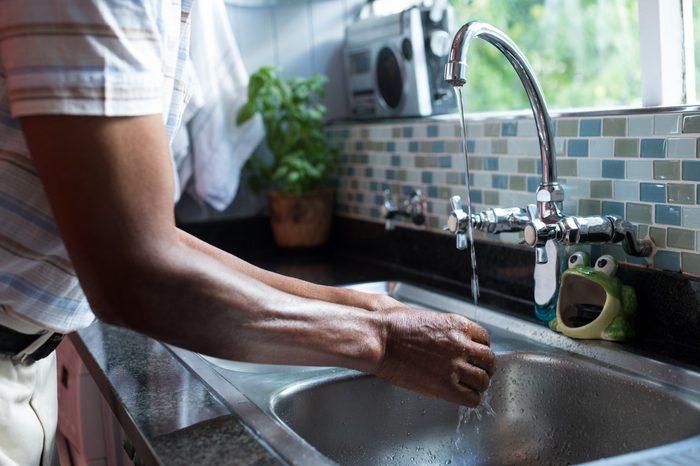 Midsection of man washing hands at sink by window