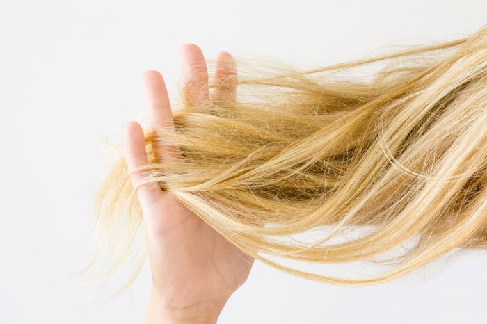 Woman's hand holding dry, blonde, tangled hair on the light gray background. Hair problem and solution. Daily women's issues.