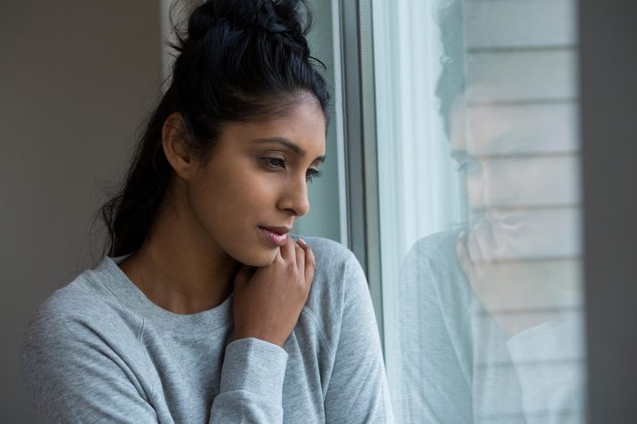 Thoughtful woman looking through window at home