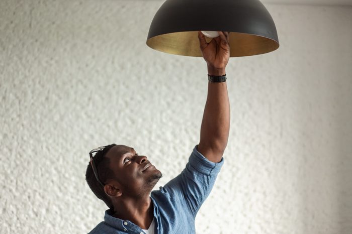 African man changing light bulb in coffee shop , installing a fluorescent light bulb