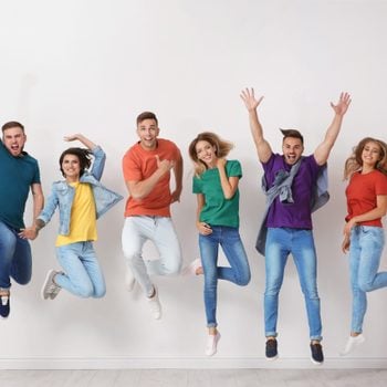 Group of young people in jeans and colorful t-shirts jumping near light wall