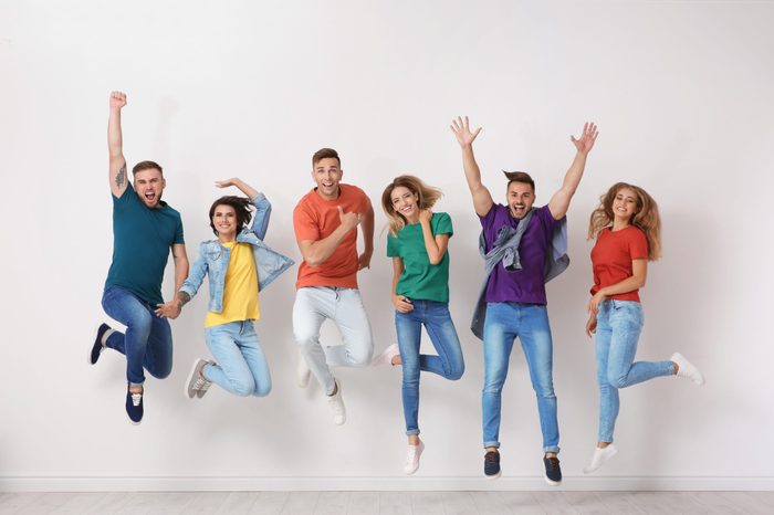Group of young people in jeans and colorful t-shirts jumping near light wall