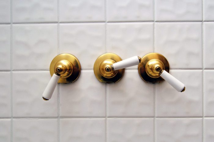 Three golden shower valve handles ona big white empty tile shower room