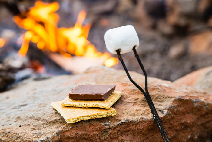 Graham crackers, chocolate, and marshmallow in front of a campfire ready to make s'mores.