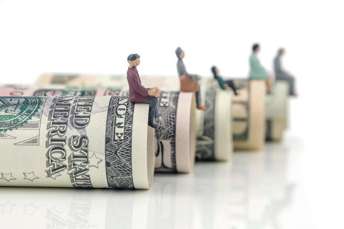 miniature figurines sitting on the edge of us dollar banknotes on white background