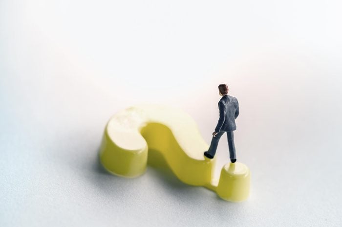 Business and working concept. Businessman miniature figure walking on yellow plastic question mark symbol