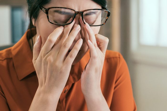stressed asian female architect having headache working in office. young girl engineer in glasses rubbing eyes painful sick tired exhausted hardworking. overwork interior designer massage nose bridge