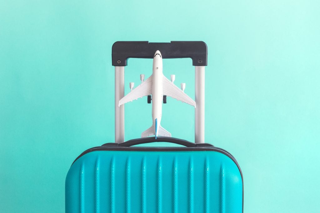 Suitcase and airplane model on pastel green background minimal creative travel concept