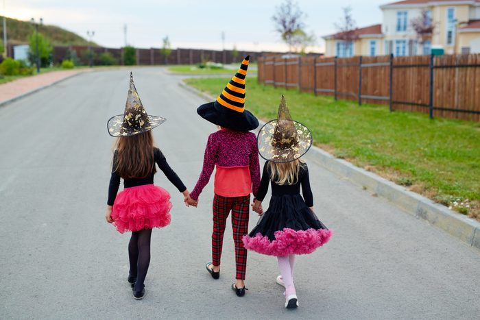 Rear view of little witches holding by hands while walking down road