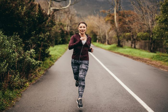 Portrait of fit young woman running on road in morning. Female jogging outdoors in morning.