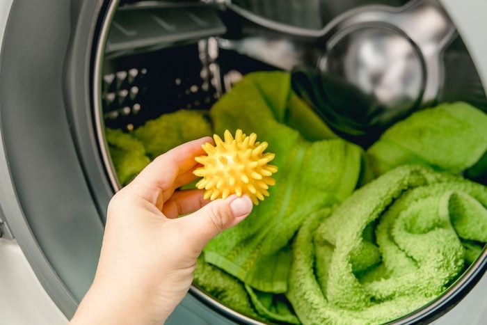 Hand holding yellow dryer ball in front of dryer machine filled with green towels
