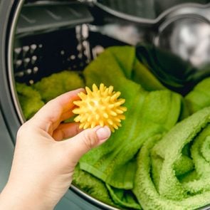 Hand holding yellow dryer ball in front of dryer machine filled with green towels