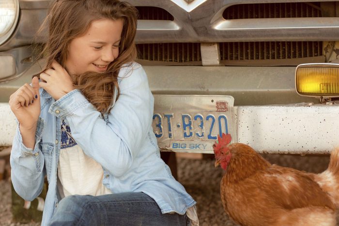 a girl, smiling, recoils from the chicken next to her