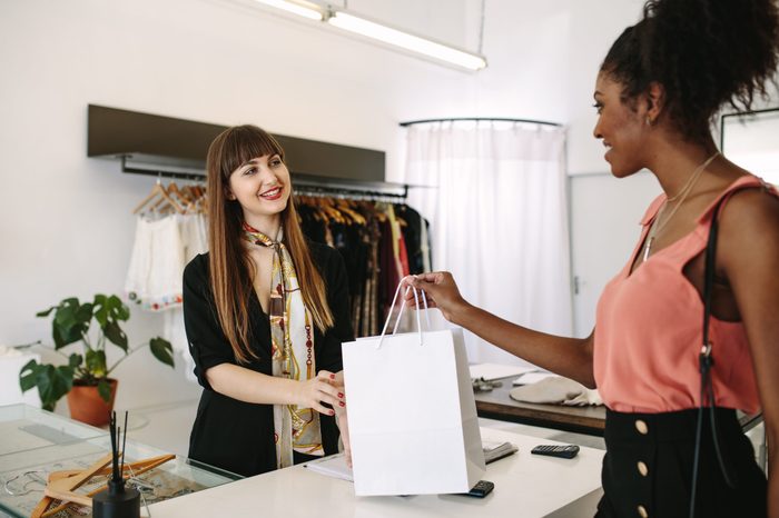 Customer shopping designer wear at a fashion boutique. Woman entrepreneur handing over shopping bag to the customer.