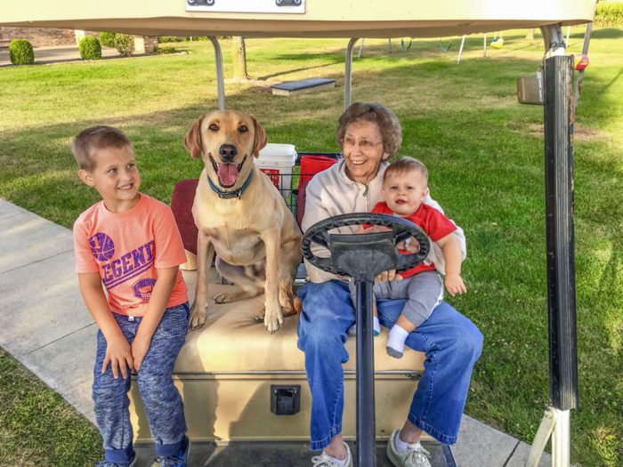 grandmother with two grandkids and a dog sit in a golf cart
