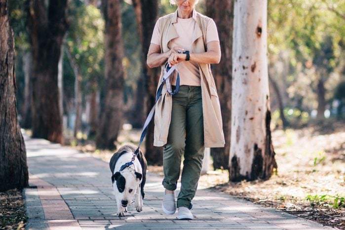 mature woman enjoying walk in nature with dog and checking texts on smartwatch