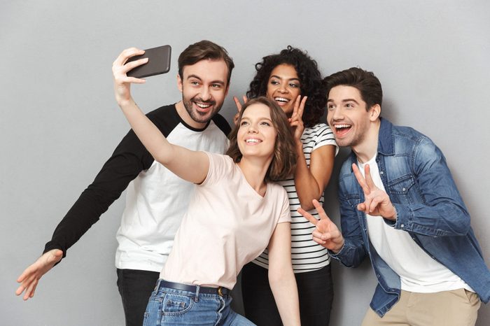 Photo of happy group of friends standing isolated over grey wall background looking aside make a selfie.