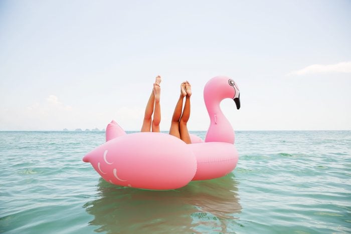 Summer lifestyle funny image of two pretty girls friends having fun on air mattress in the ocean. Doing yoga and having fun. Legs up in the air. Positive emotions, bright colors 