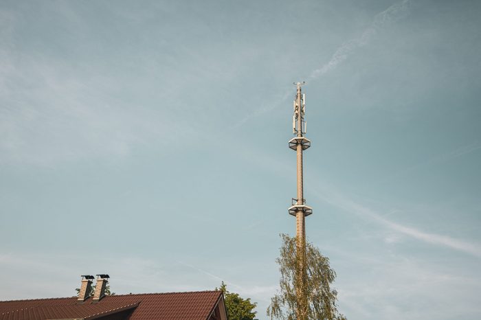 a radio mast for the mobile phone network towers above a residential building into the blue sky in a residential area
