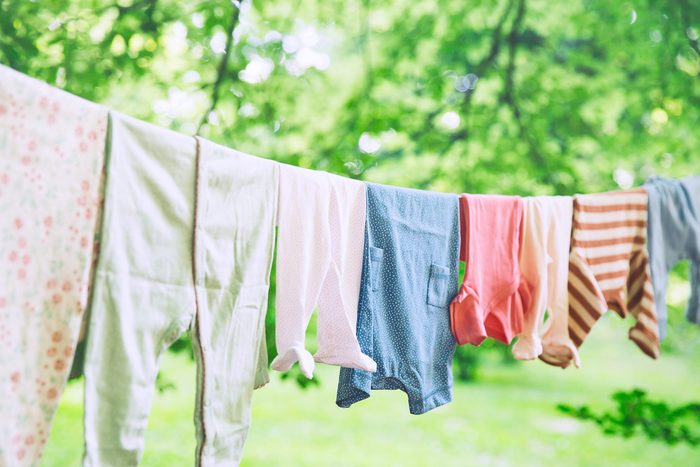 Baby cute clothes hanging on the clothesline outdoor. Child laundry hanging on line in garden on green background. Baby accessories.