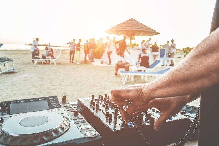 Dj mixing at sunset beach party in summer vacation outdoor - Disc jockey hands playing music for tourist people in chiringuito kiosk bar - Event, music and fun concept - Focus on left hand 