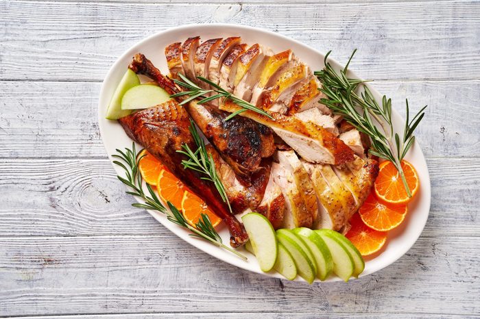 View from above on sliced roast duck served with rosemary, green apple, orange on a white plate on a white wooden table, close-up