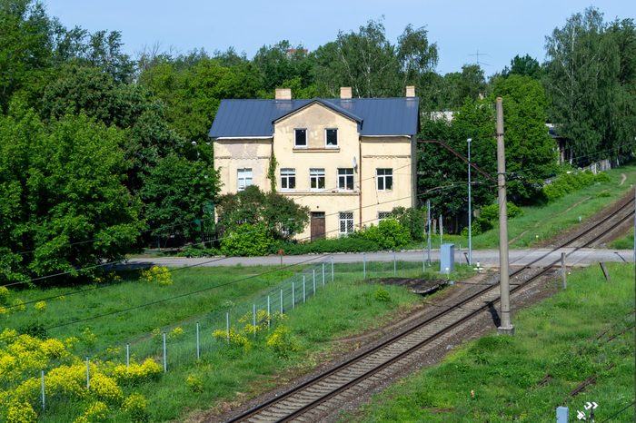 House near train rails and iron crossing. House with green trees and yellow flower