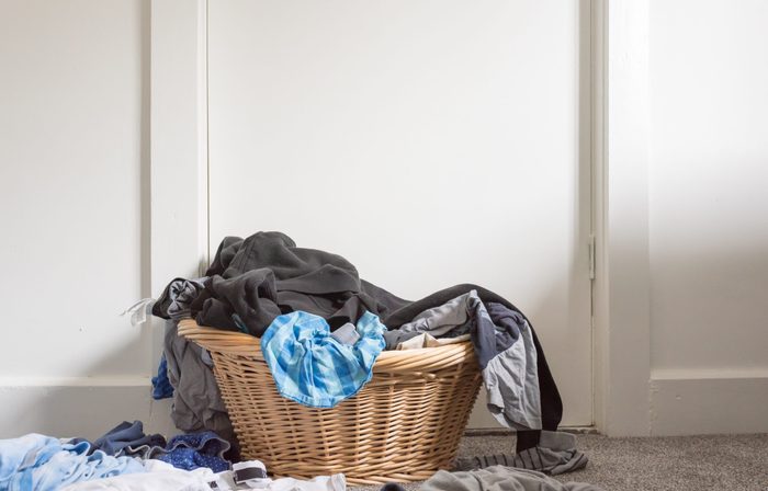 Low angle view of wicker basket with overflowing pile of blue and black clothing against white wall (selective focus)