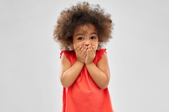 childhood, expression and emotion concept - confused little african american girl covering mouth by hands over grey background