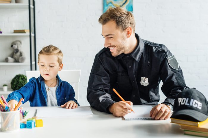 happy young father in police uniform and his little son drawing together at home