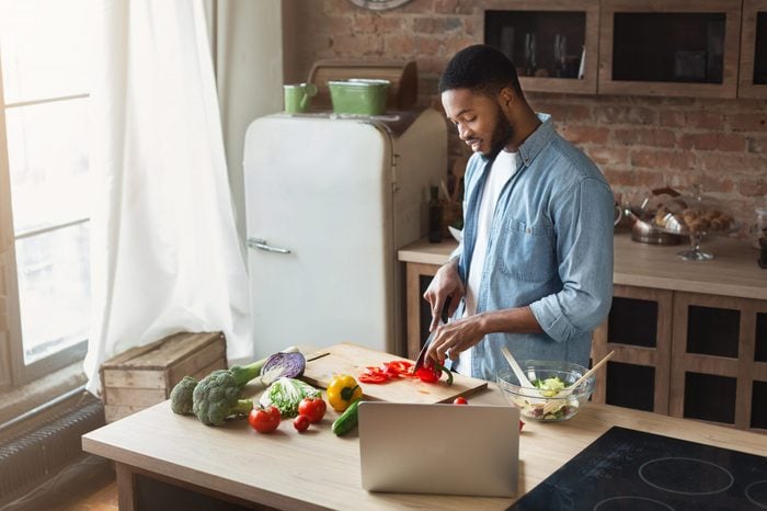 African-american man preparing vegetable salad in loft kitchen